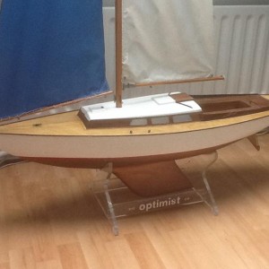 Graupner Optimist een weekend na aankoop, ontdaan van alle losse en beschadigde onderdelen. Het resultaat is een casco met een strakke romp met herstelwerk bij de spiegel maar met een goede romp/dek- en romp/kielverbinding, een net dek met een voetlijst, kikkers, klampen en boegbeslag, een kuip en kajuitopbouw met wat schoonheidsfoutjes en een gave houten mast met bijbehorende giek en boom met alle beslag. De fok is heel maar opgerekt, opgebleekt en daarmee uitgezeild. Het grootzeil ronduit gaar. Het roerblad ontbreekt maar de roerkoning is recht. Het kajuitdak in al zijn simpelheid dekt het geheel af.