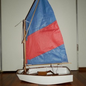 Optimist jeugdzelboot met het tweede zeil, waarbij de giek lager uitkomt en de spriet de tophoek hogers opsteekt. Het zeiltje blijft zelfs zonder zeillatten aan het achterlijk mooi gevormd, en met een kunstmatig gevormde wind vormde het zich goed. Straks aan het water denk ik dat er met behulp van neerhouder, onderlijkstrekker en spriettakel een mooi trimbaar zeitje op deze modeloptimist staat!