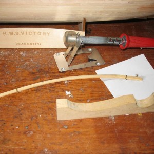 Buiggereedschap. Het latje ligt plat op de werktafel, tussen spijkertjes geklemd, en is horizontaal gebogen. Met de vorm op de voorgrond kan hij ook daarna verticaal worden gebogen. Door de hete bout is het dan ook meteen droog en blijft in vorm staan.