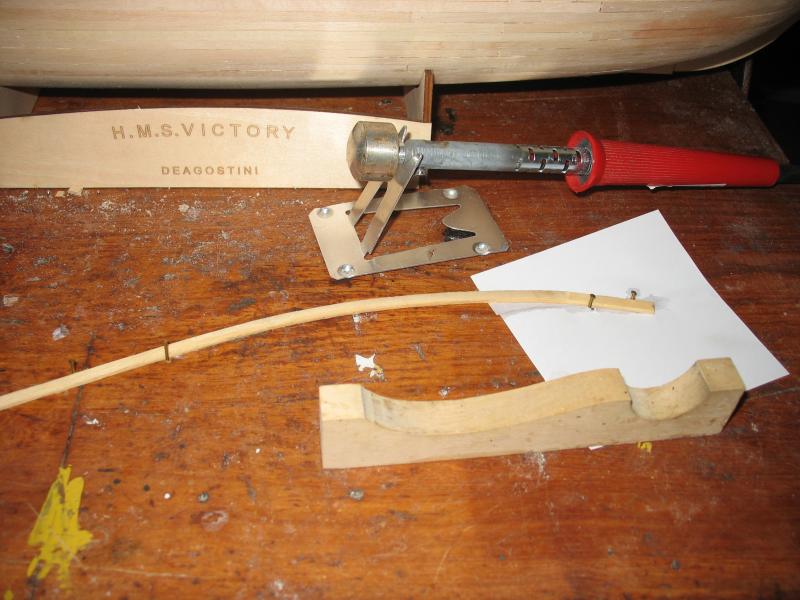 Buiggereedschap. Het latje ligt plat op de werktafel, tussen spijkertjes geklemd, en is horizontaal gebogen. Met de vorm op de voorgrond kan hij ook daarna verticaal worden gebogen. Door de hete bout is het dan ook meteen droog en blijft in vorm staan.