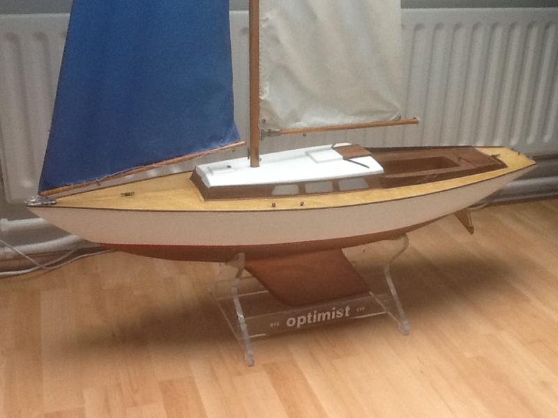 Graupner Optimist een weekend na aankoop, ontdaan van alle losse en beschadigde onderdelen. Het resultaat is een casco met een strakke romp met herstelwerk bij de spiegel maar met een goede romp/dek- en romp/kielverbinding, een net dek met een voetlijst, kikkers, klampen en boegbeslag, een kuip en kajuitopbouw met wat schoonheidsfoutjes en een gave houten mast met bijbehorende giek en boom met alle beslag. De fok is heel maar opgerekt, opgebleekt en daarmee uitgezeild. Het grootzeil ronduit gaar. Het roerblad ontbreekt maar de roerkoning is recht. Het kajuitdak in al zijn simpelheid dekt het geheel af.